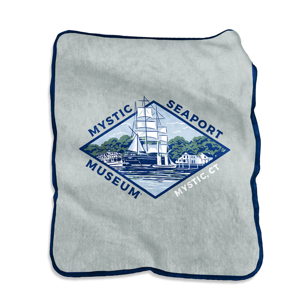 The Mystic Seaport Museum Raschel Blanket is light gray with dark blue trim, featuring a sailing ship and waterfront buildings. "Mystic Seaport Museum" and "Mystic, CT" appear in a diamond shape around the illustration.